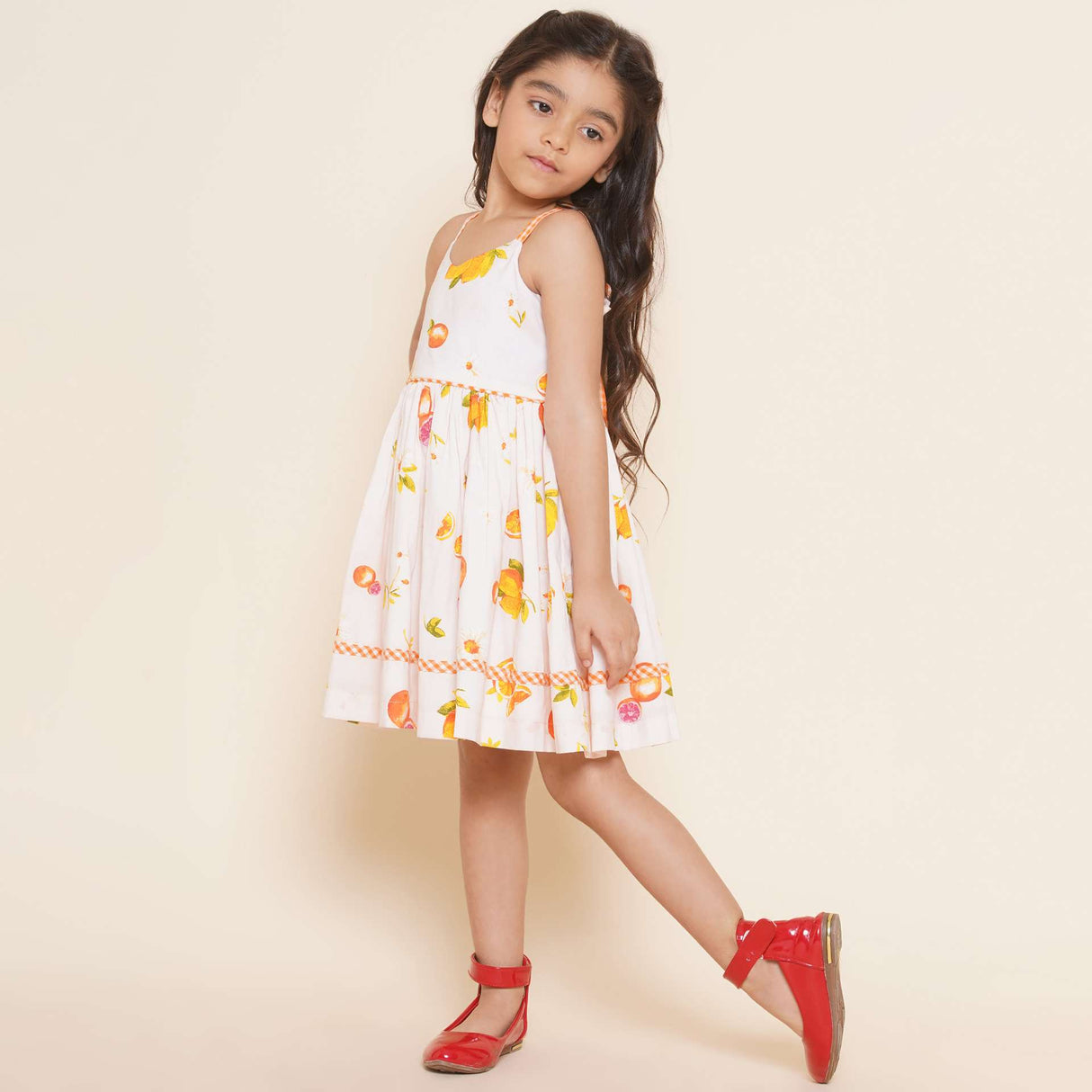 A little girl in pink vibrant fruit print dress with lemons, tangerines and daisies and orange gingham trims