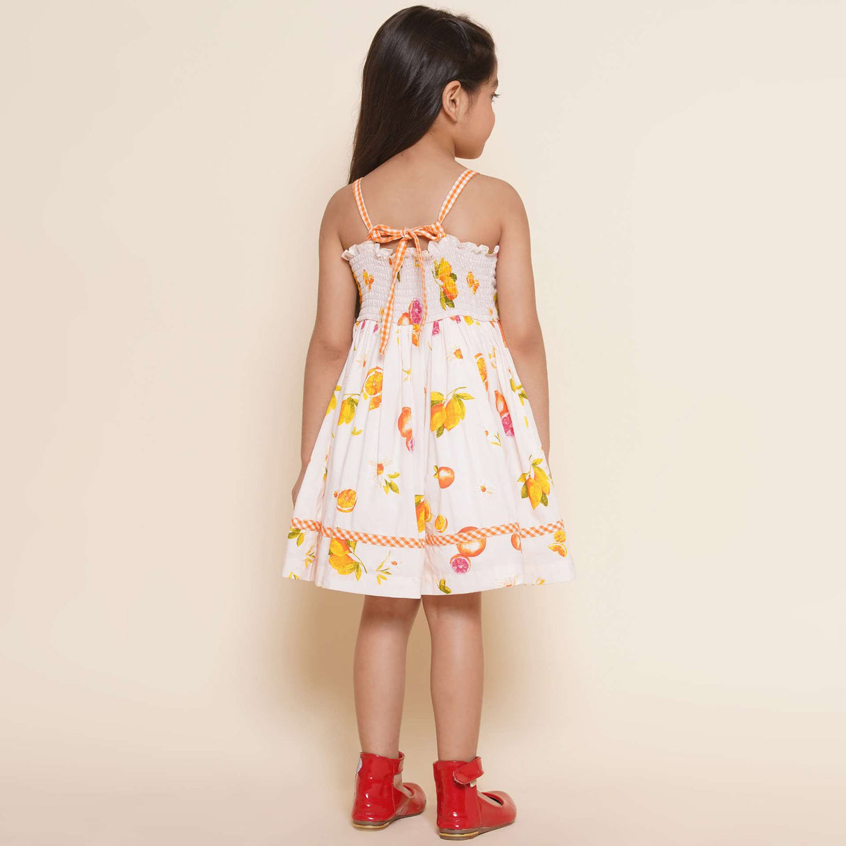 A little girl in pink vibrant fruit print dress with lemons, tangerines and daisies and orange gingham trims