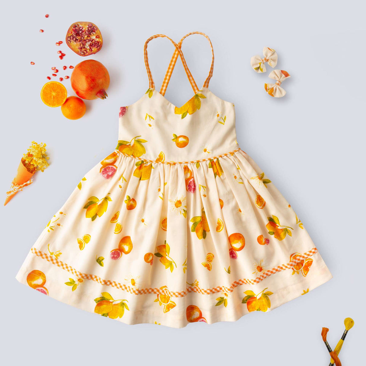 Flatlay of pink vibrant fruit print dress with lemons, tangerines and daisies and orange gingham trims