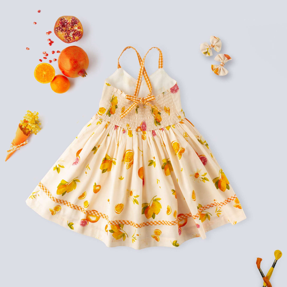 Flatlay of pink vibrant fruit print dress with lemons, tangerines and daisies and orange gingham trims