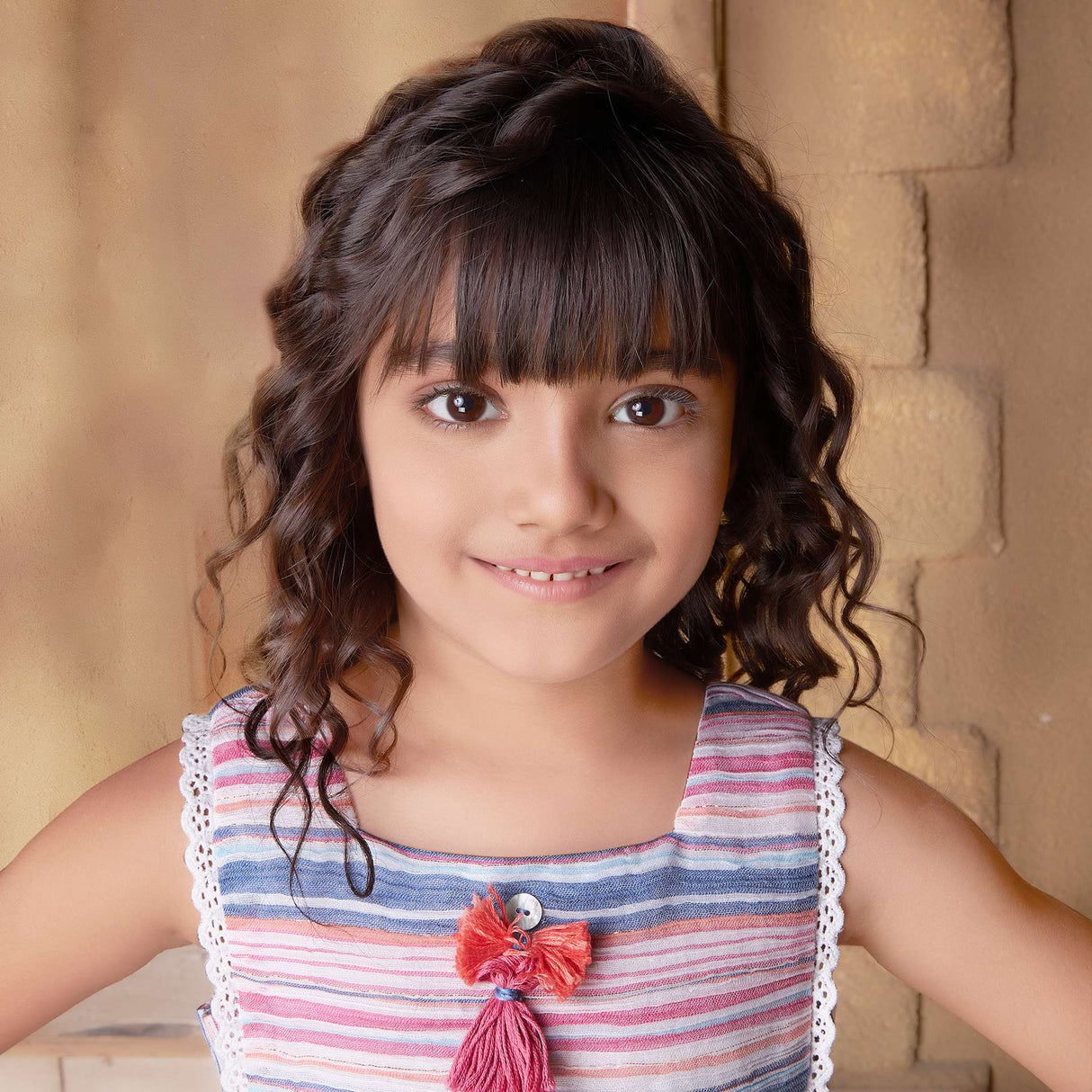 Close up of a little girl in sleeveless multi-color stripe dress with side ties, lace trims and a decorative thread bow