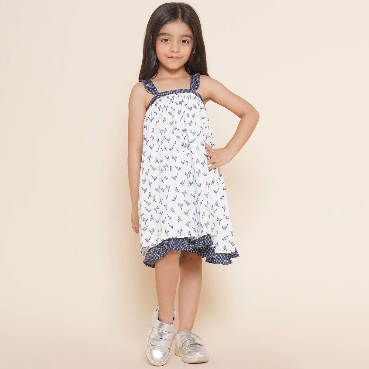 A little girl in strappy shoulder dress with blue bird print and tiny ruffles on the shoulder straps in navy dot fabric