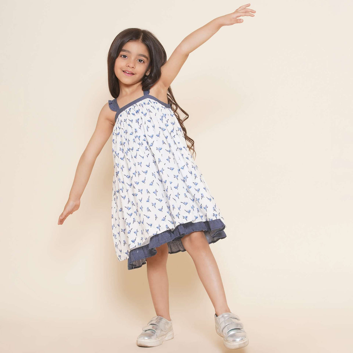 A little girl in strappy shoulder dress with blue bird print and tiny ruffles on the shoulder straps in navy dot fabric