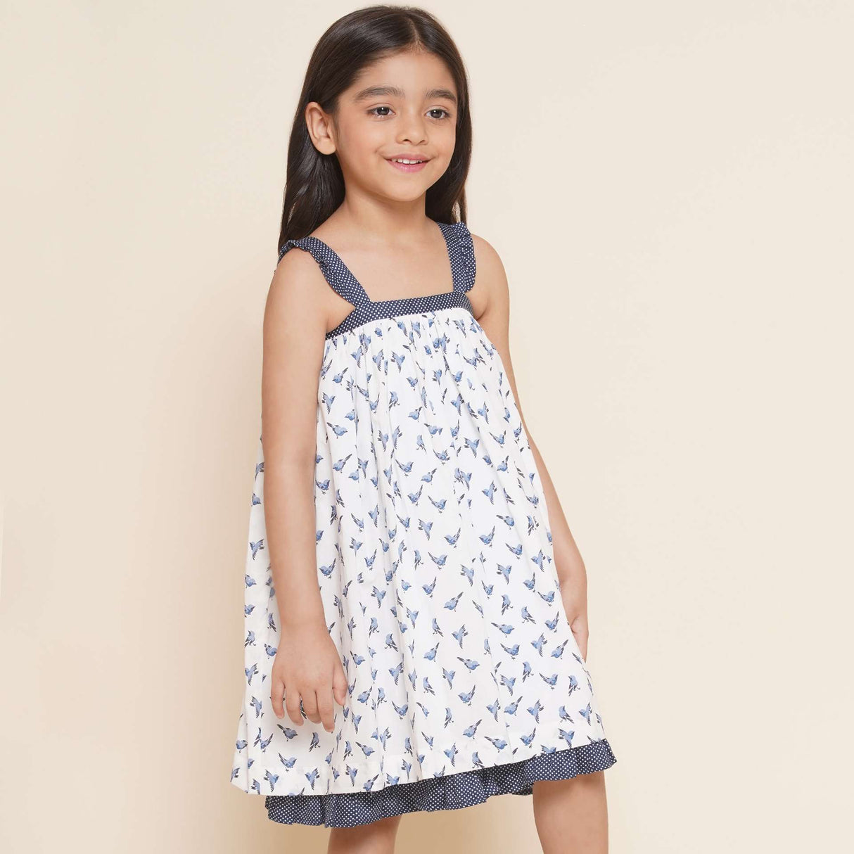 A little girl in strappy shoulder dress with blue bird print and tiny ruffles on the shoulder straps in navy dot fabric