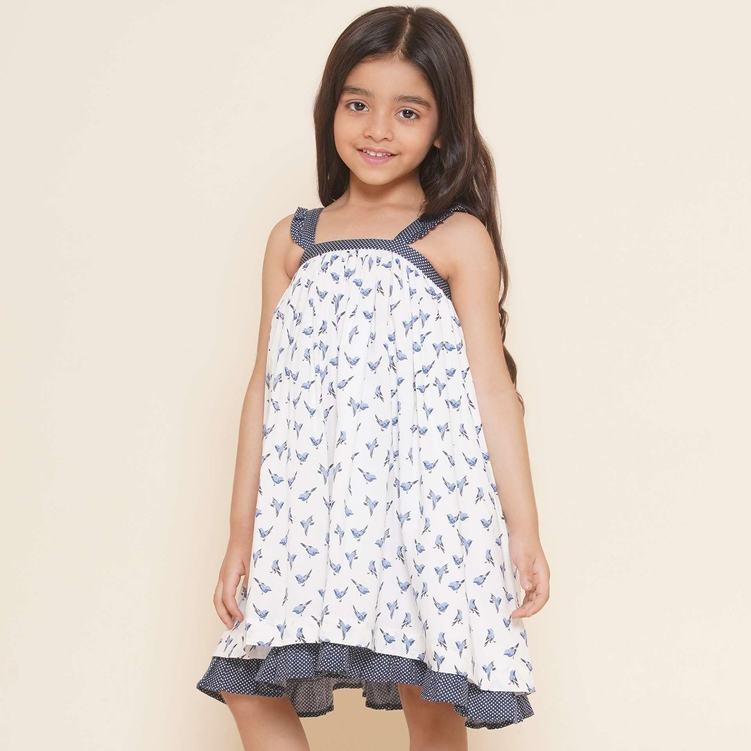 A little girl in strappy shoulder dress with blue bird print and tiny ruffles on the shoulder straps in navy dot fabric