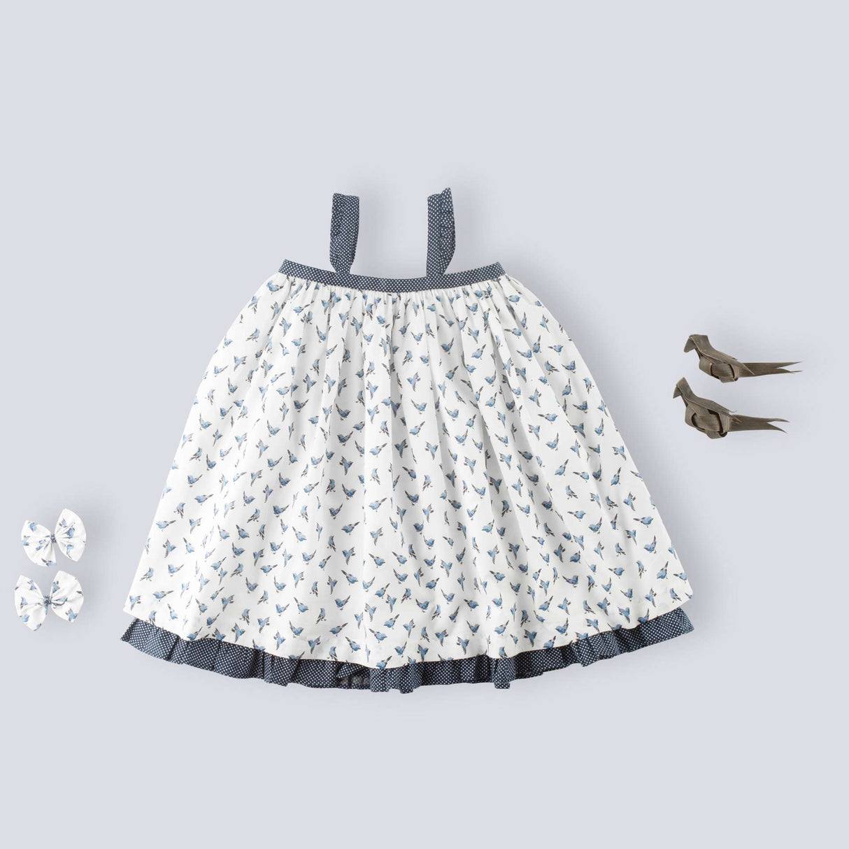 Flatlay of strappy shoulder dress with blue bird print and tiny ruffles on the shoulder straps in navy dot fabric