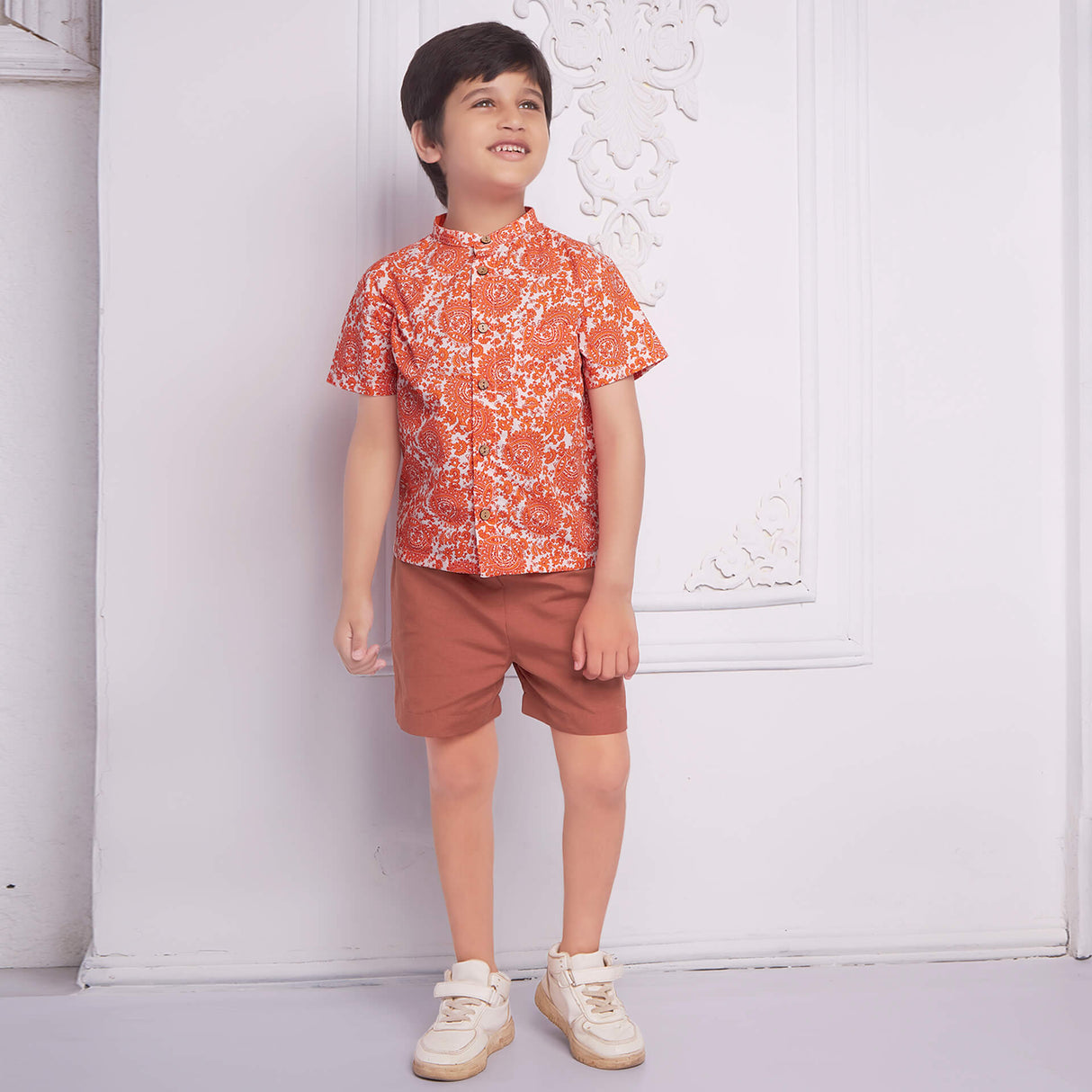 Smiling boy wearing an orange floral printed mandarin collared shirt matched with rust short