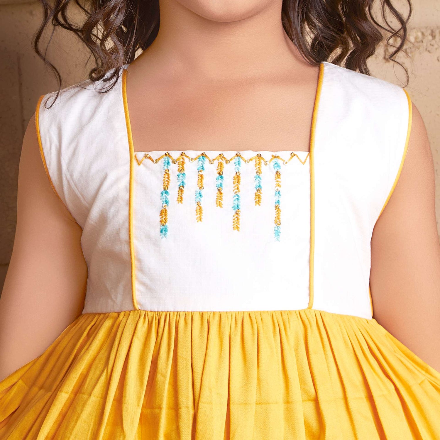 Sleeveless gold dress featuring a floral “toran”, hand embroidered with beads and sequins on an ivory bodice