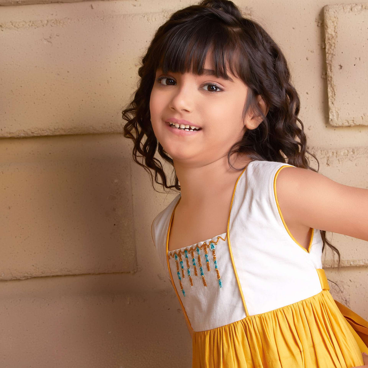 Close-up of a young girl wearing sleeveless golden yellow dress with a 'Toran' hand embroidered yoke and hem ruffles