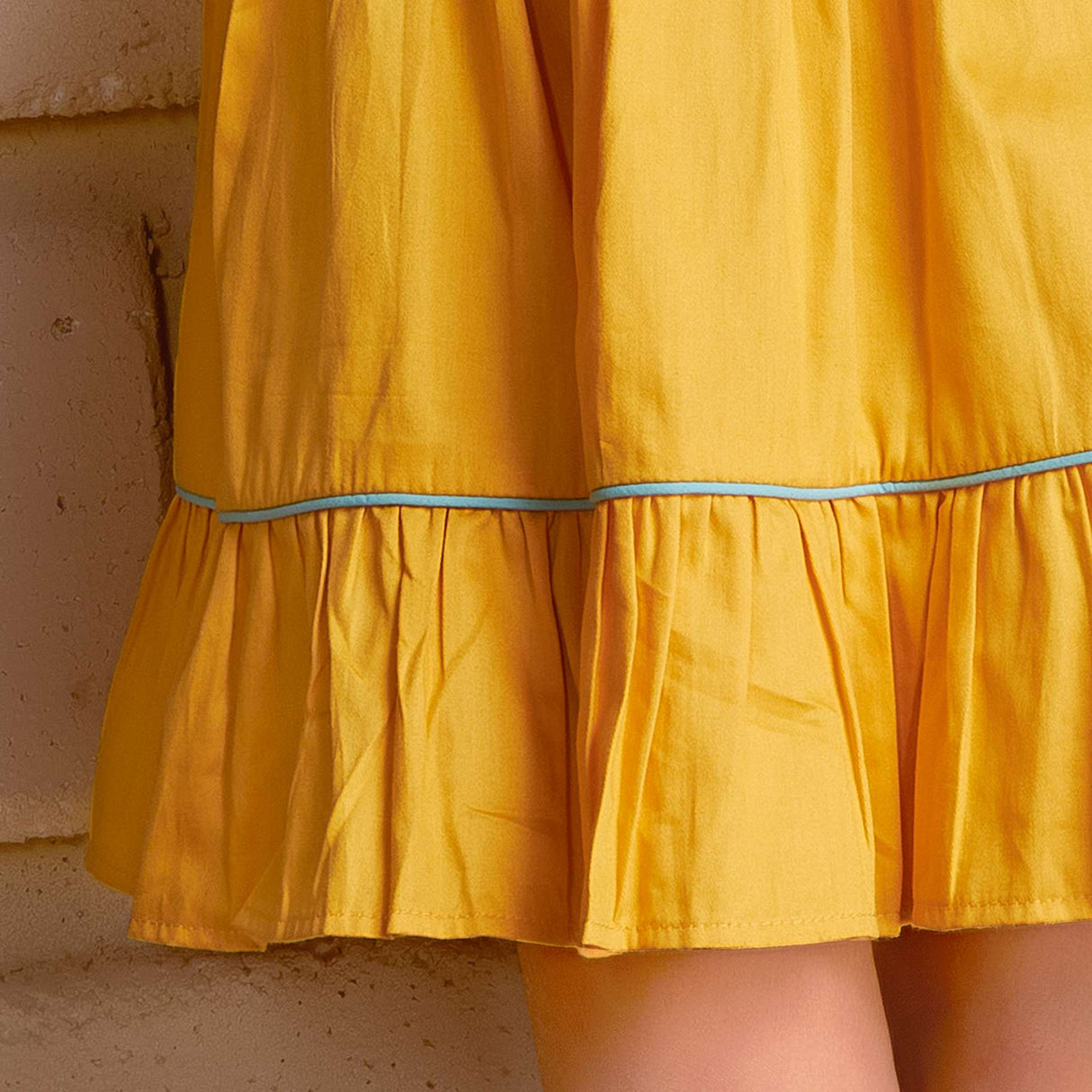 Close-up of ruffled hem of sleeveless golden yellow dress with a 'Toran' hand embroidered yoke