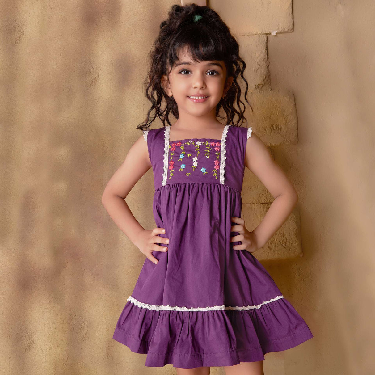 A little girl in magenta dress with hand embroidered floral garlands, embellished with woven lace and wooden buttons