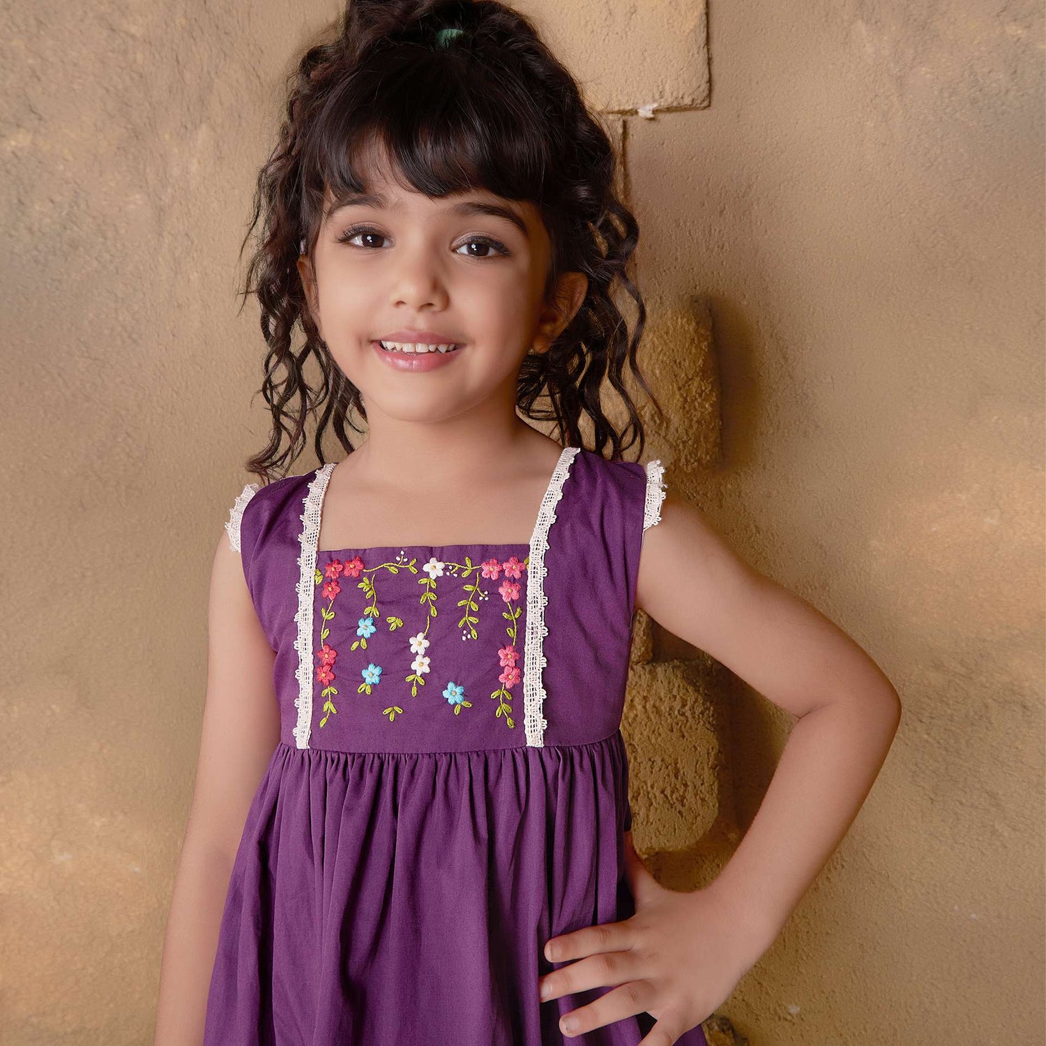 A little girl in magenta dress with hand embroidered floral garlands, embellished with woven lace and wooden buttons