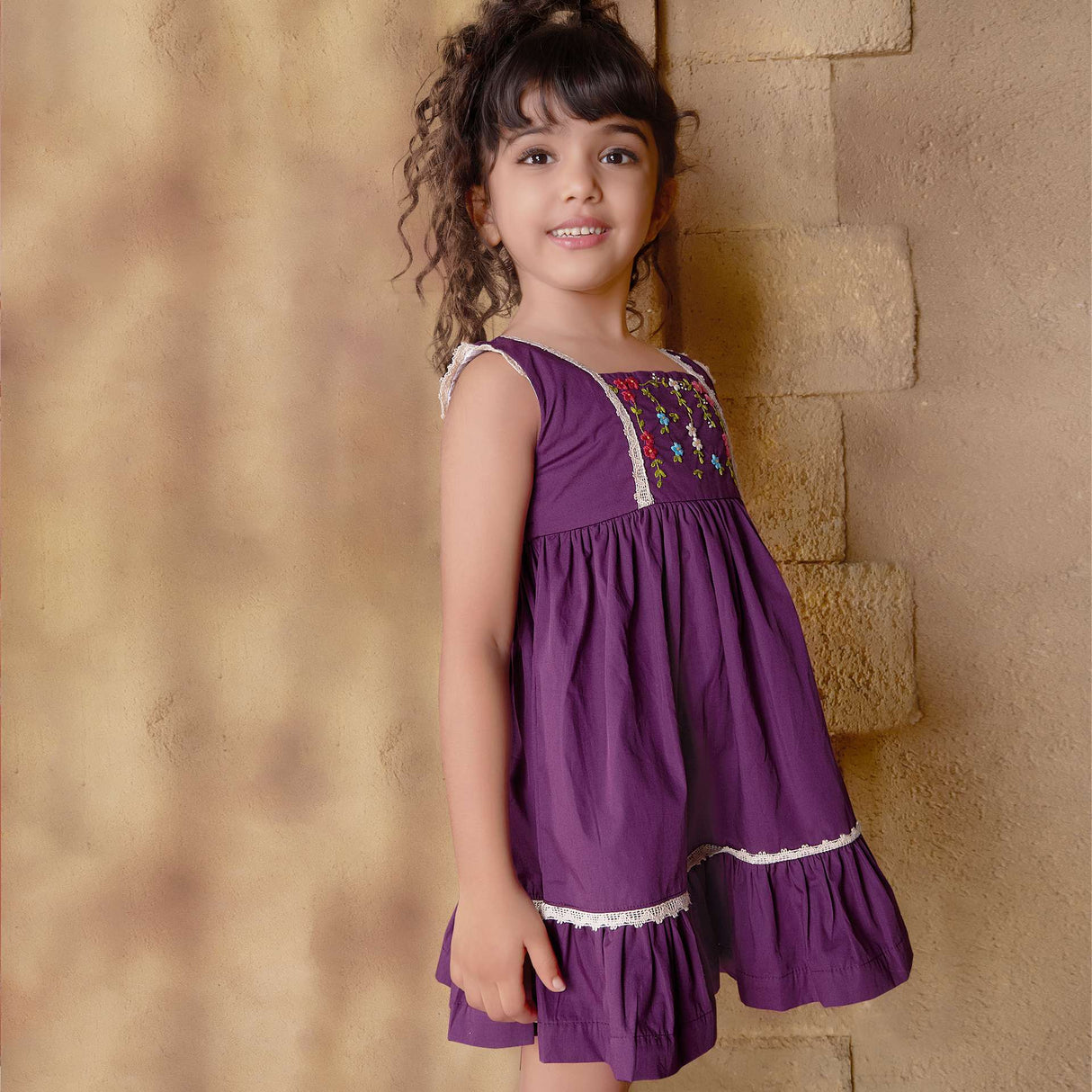 A little girl in magenta dress with hand embroidered floral garlands, embellished with woven lace and wooden buttons