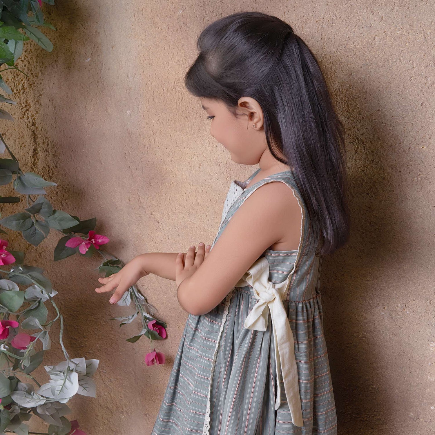 A young girl showcasing striped sleeveless dress with charming side bows and delicate lace trims