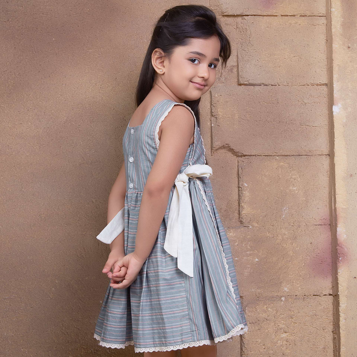 A young girl showcasing striped sleeveless dress with charming side bows and delicate lace trims