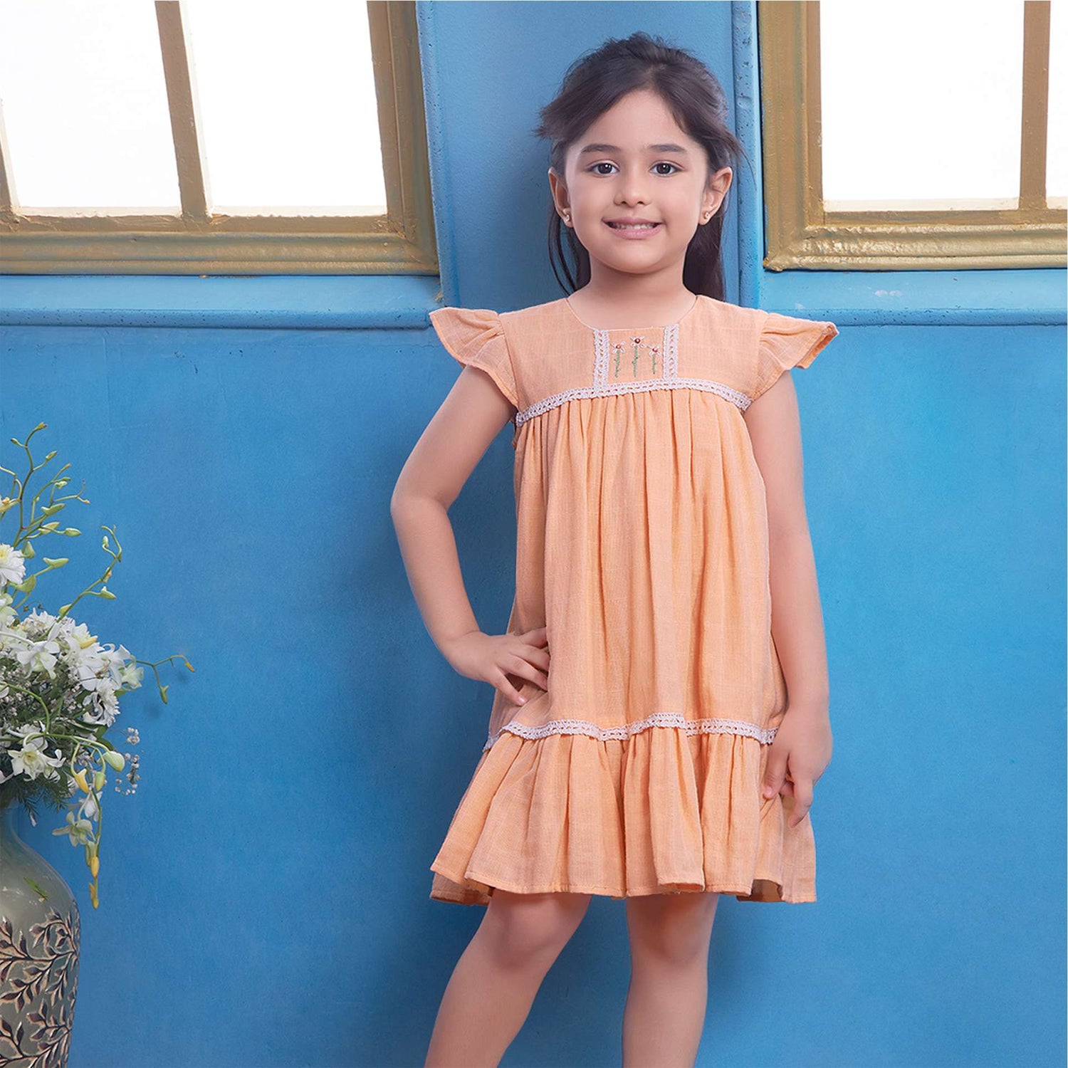 A young girl in peach gauze dress with hand-embroidered flowers in the yoke, ivory lace trims and a ruffled hem