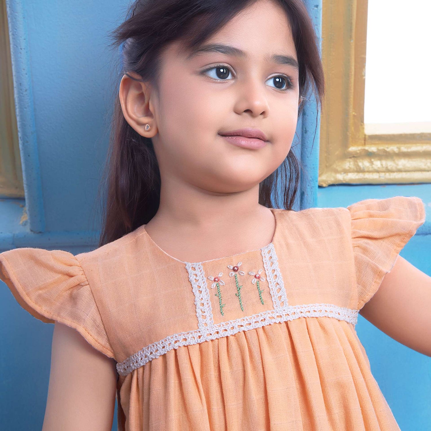 A young girl in peach gauze dress with hand-embroidered flowers in the yoke, ivory lace trims and a ruffled hem