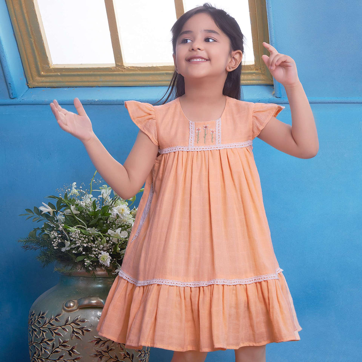 A young girl in peach gauze dress with hand-embroidered flowers in the yoke, ivory lace trims and a ruffled hem
