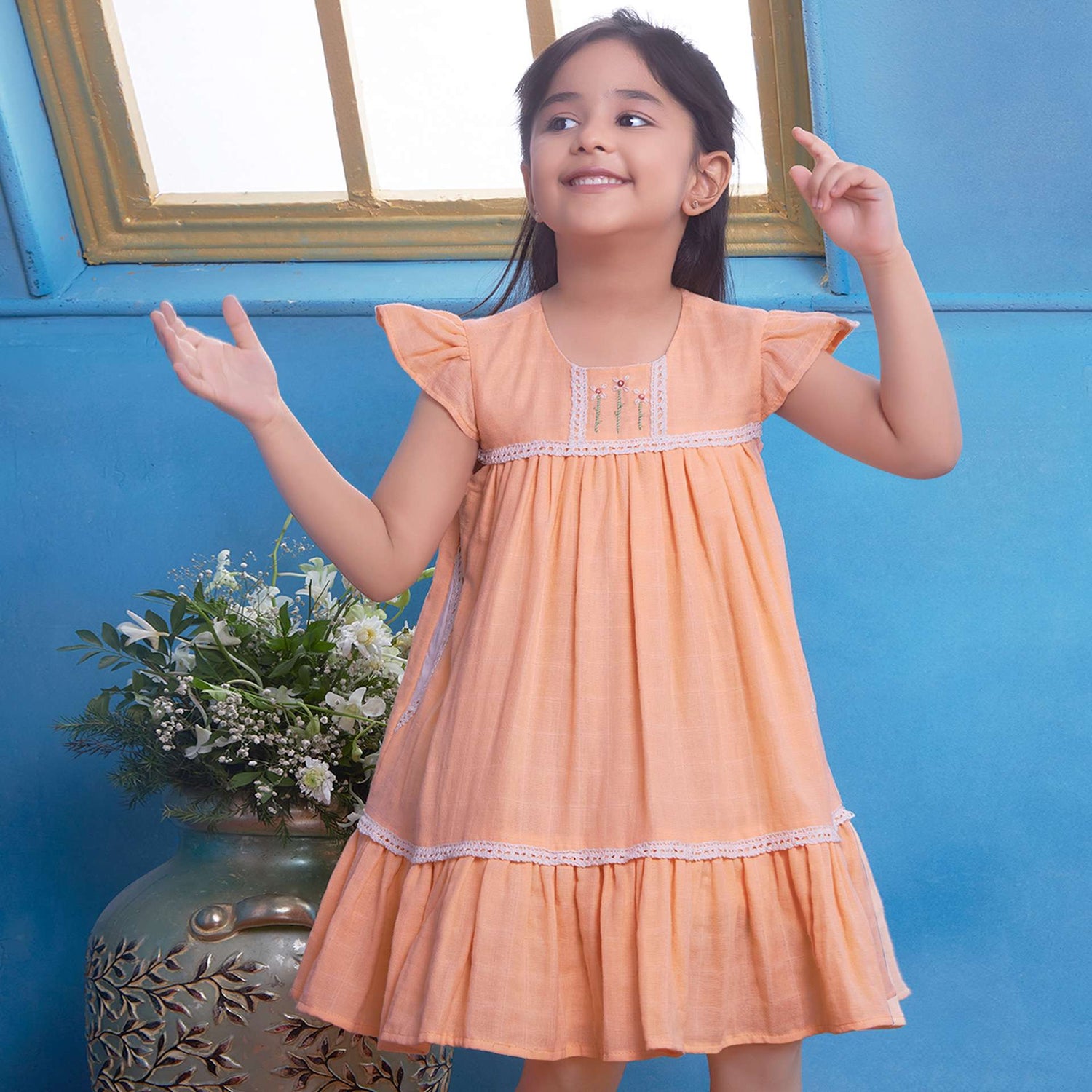 A young girl in peach gauze dress with hand-embroidered flowers in the yoke, ivory lace trims and a ruffled hem