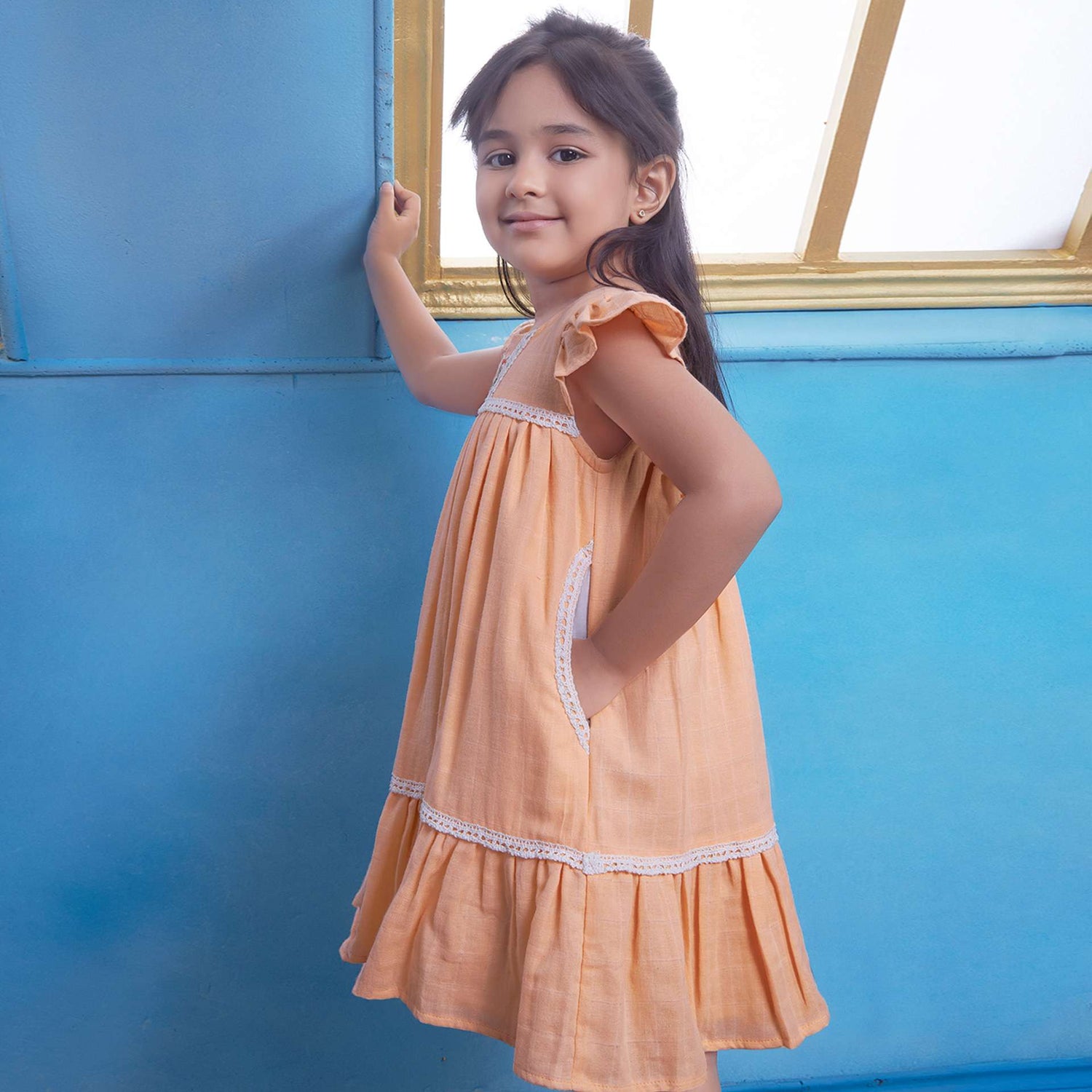 A young girl in peach gauze dress with hand-embroidered flowers in the yoke, ivory lace trims and a ruffled hemv