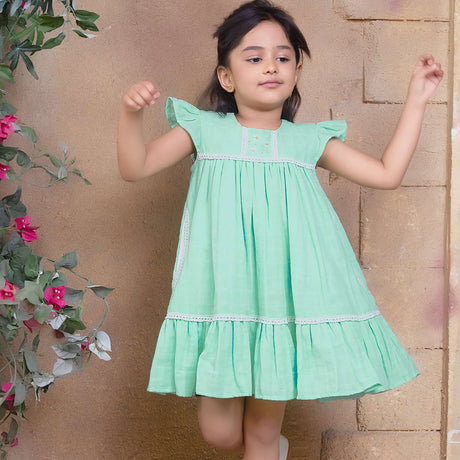 A little girl in aqua double gauze fabric dress with hand-embroidered flower details in the yoke with ivory lace trims