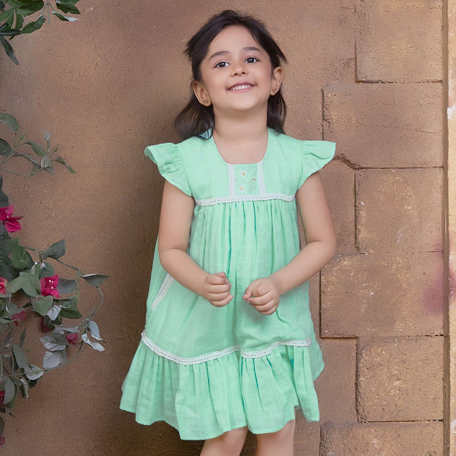A little girl in aqua double gauze fabric dress with hand-embroidered flower details in the yoke with ivory lace trims