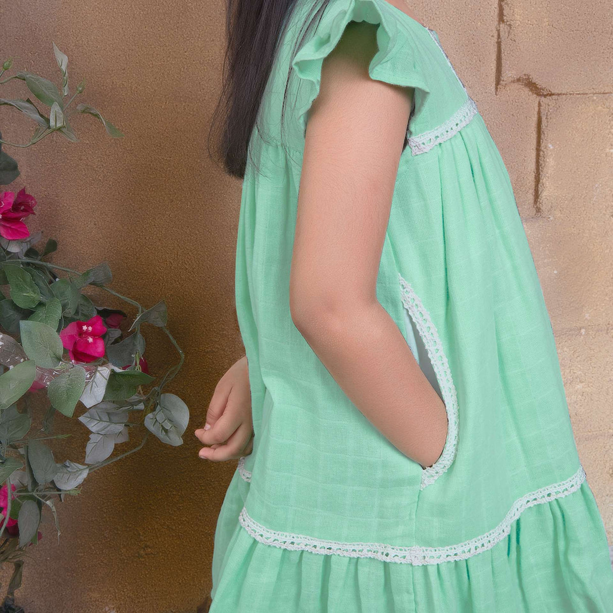 A little girl in aqua double gauze fabric dress with hand-embroidered flower details in the yoke with ivory lace trims