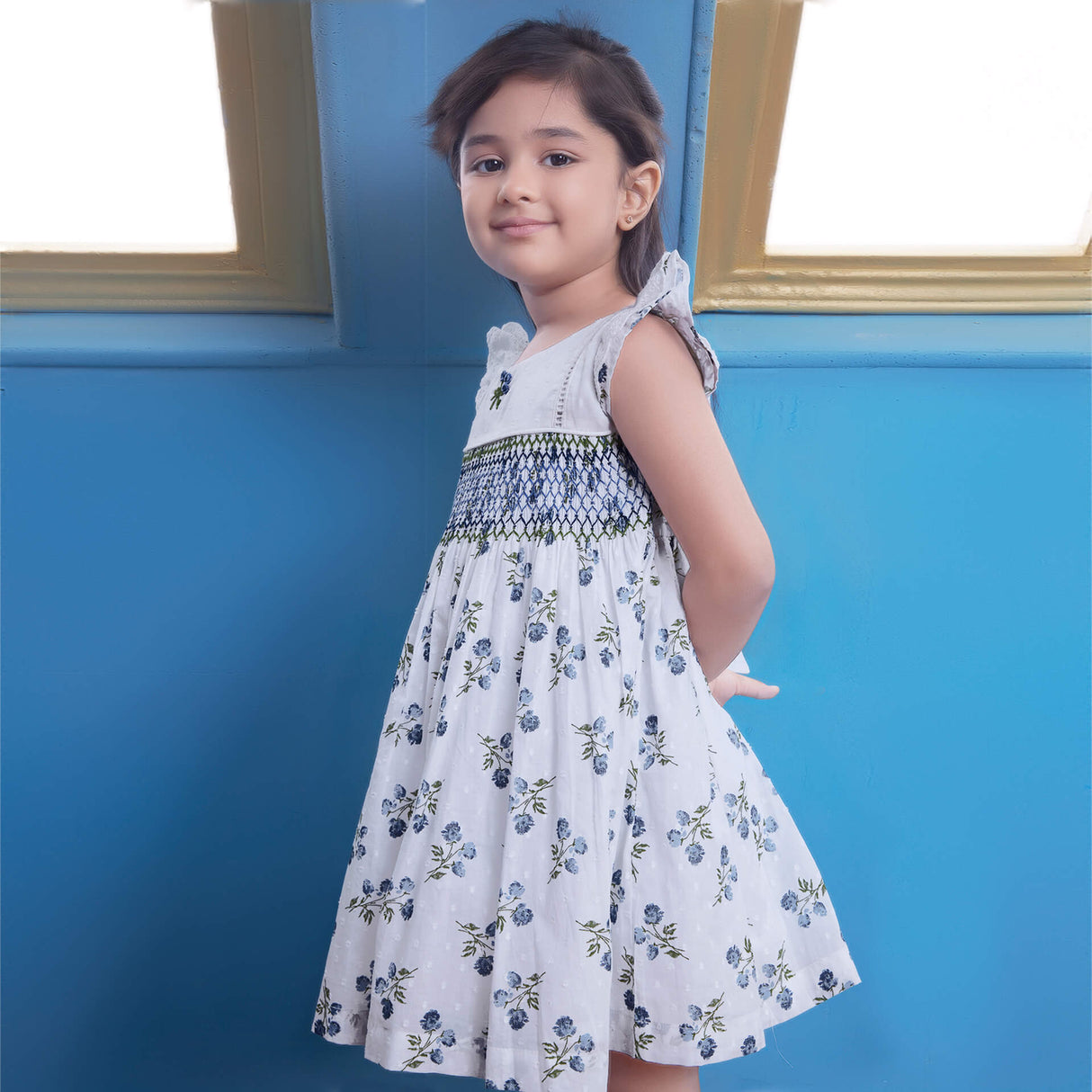 Posing from the side, a girl wears white floral printed smocked dress