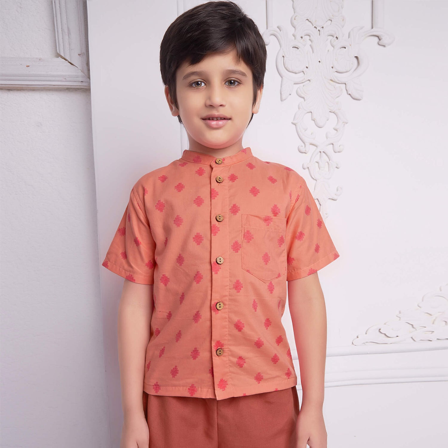 Boy wears a peach and pink print shirt with wood buttons