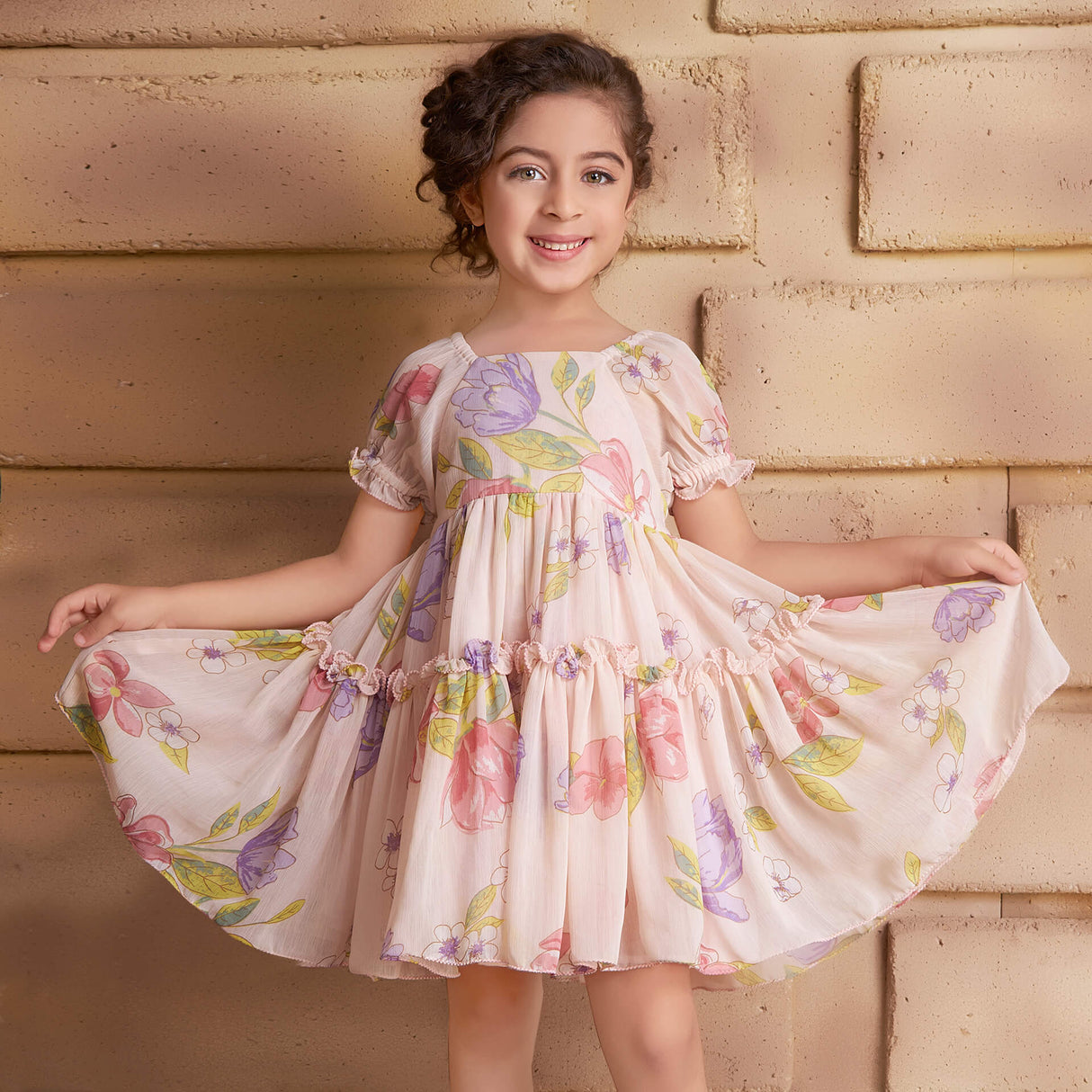 Posing in a pink chiffon dress, the girl playfully stretches the skirt with both hands
