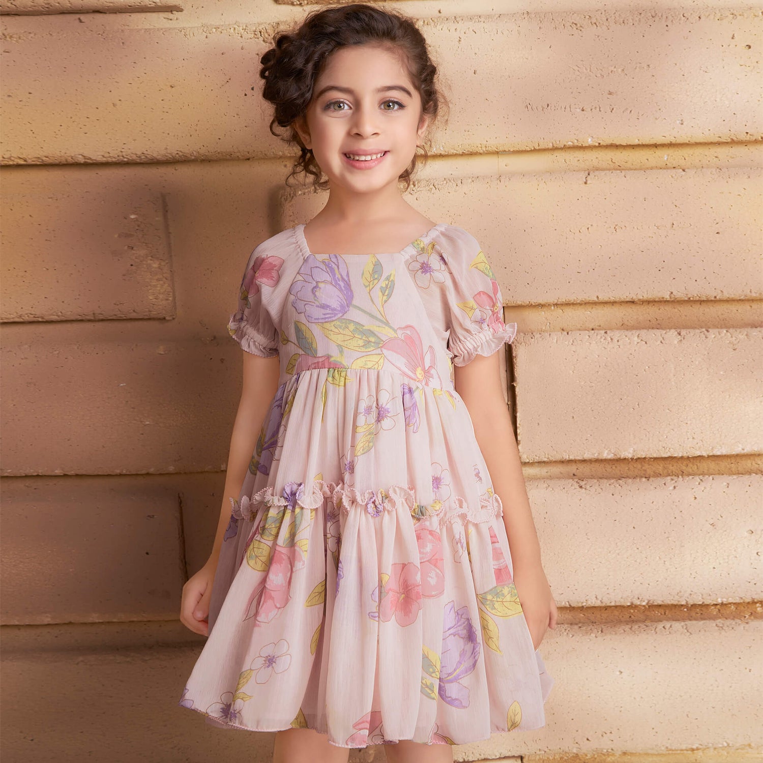 A smiling girl wearing a pink floral printed chiffon ruffle dress
