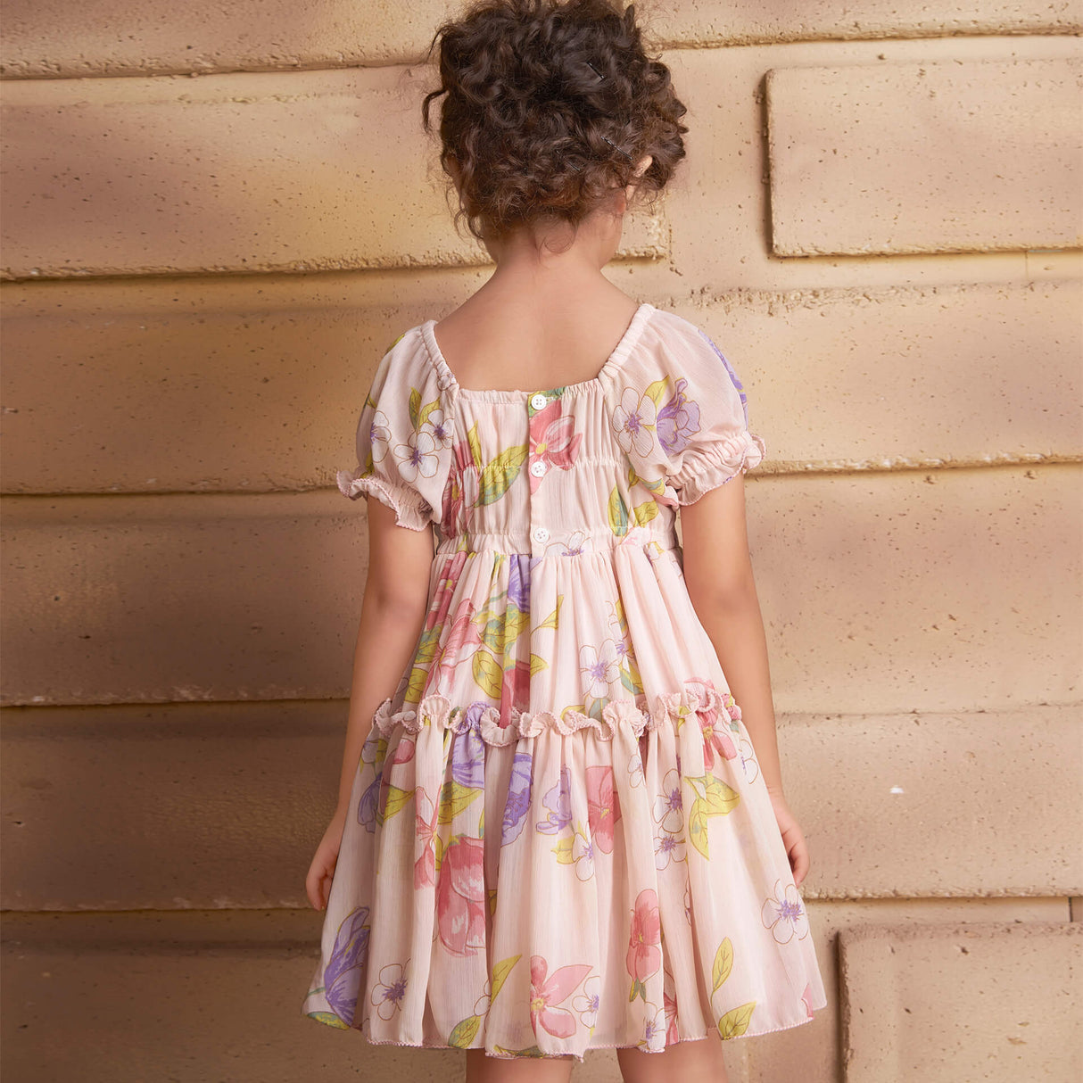 Back view of a girl wearing a pink floral printed chiffon ruffle dress