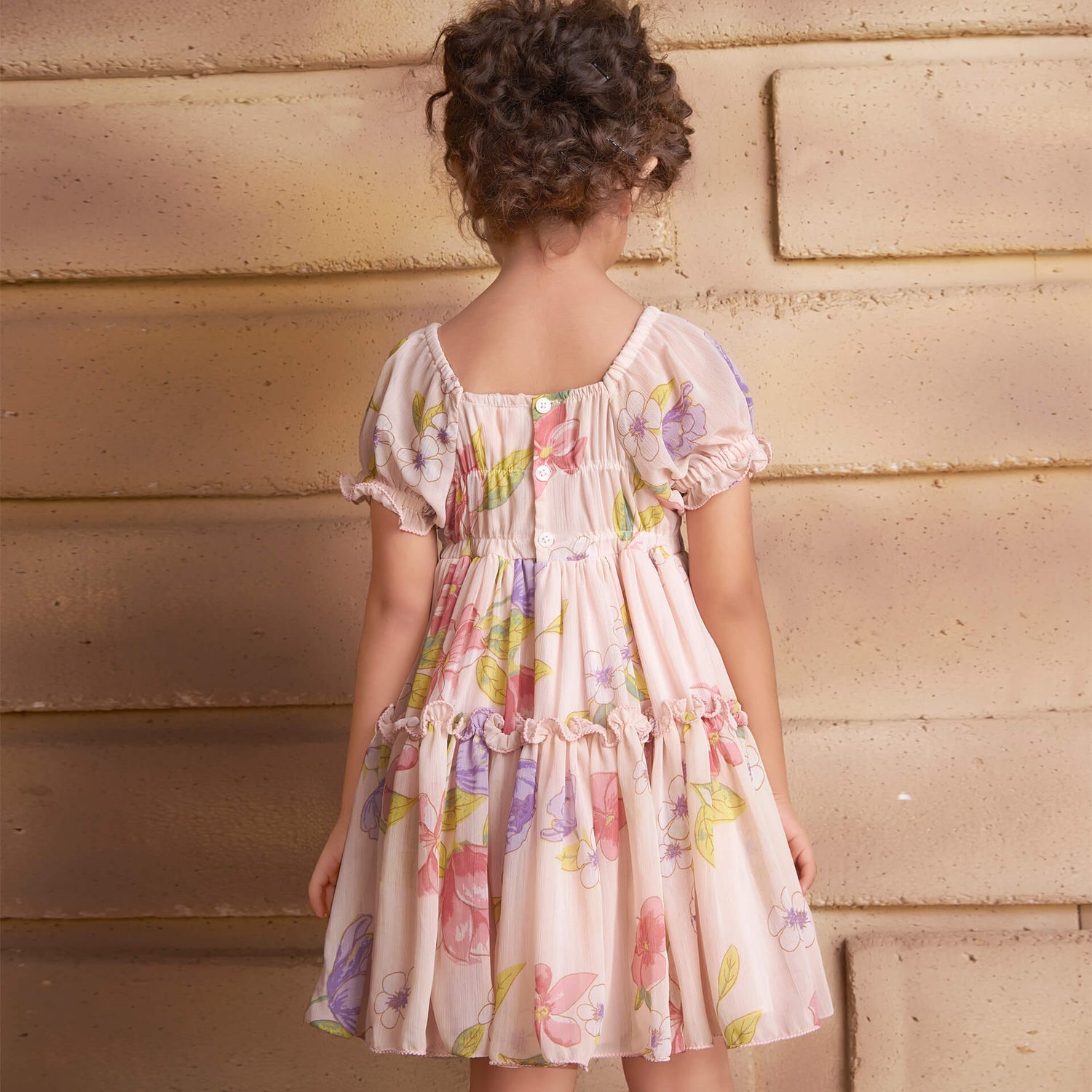 Back view of a girl wearing a pink floral printed chiffon ruffle dress