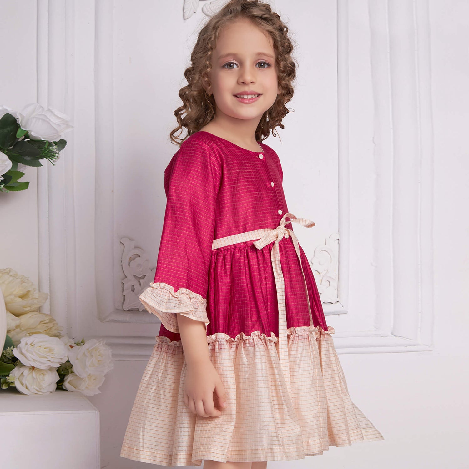 Side view of a girl posing in pink and ivory chanderi dress with front pearl buttons and a tie-up sash