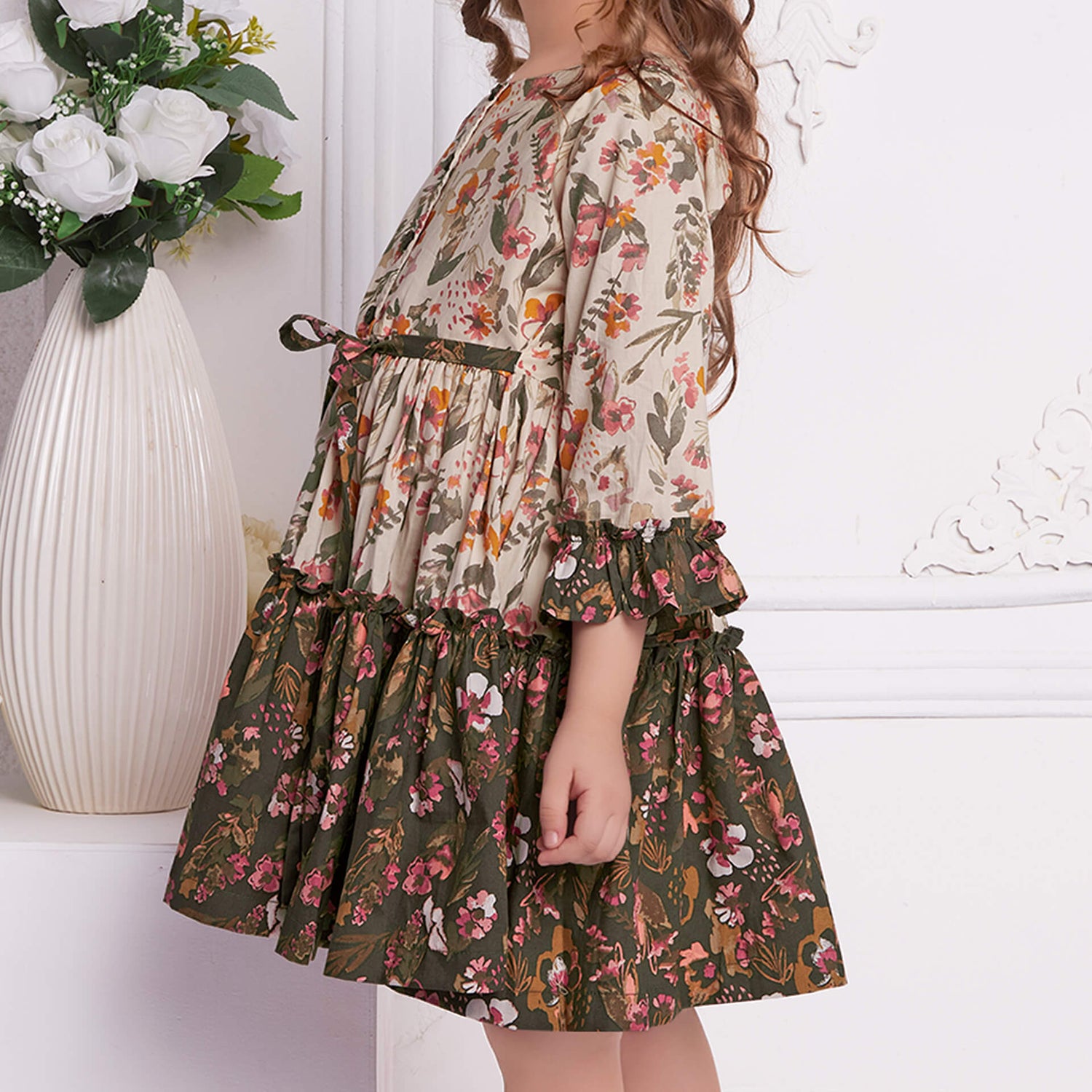 Side view of ruffle dress in contast tones with tie up sash in the front, fastened by wooden buttons