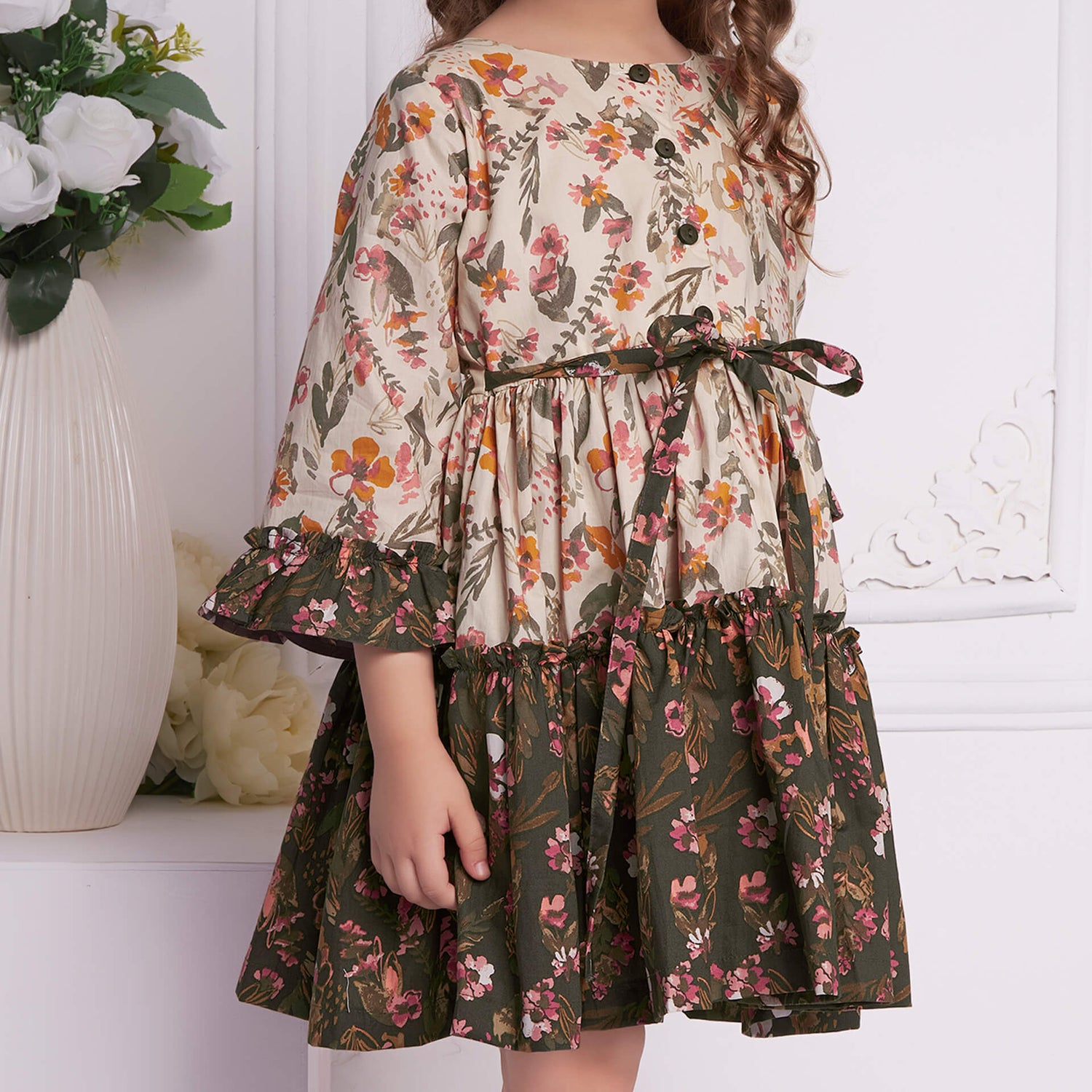 Close-up of a beige and green floral printed dress featuring a tie-up sash, wood button fastening, and ruffle details.