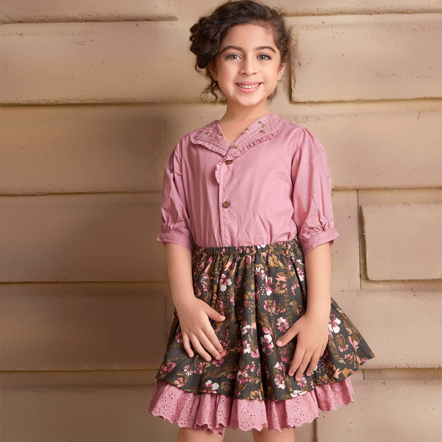 In a pink embroidered blouse and floral printed skirt, the girl smiles as she strikes a pose