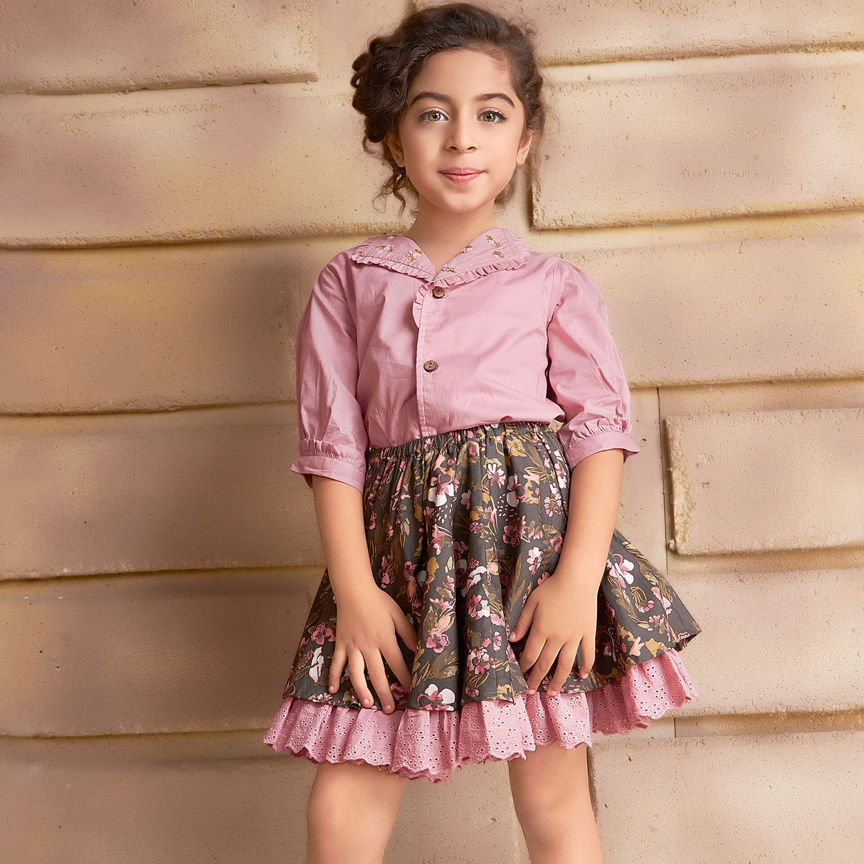 In a pink embroidered blouse and green floral printed skirt, the girl smiles as she strikes a pose