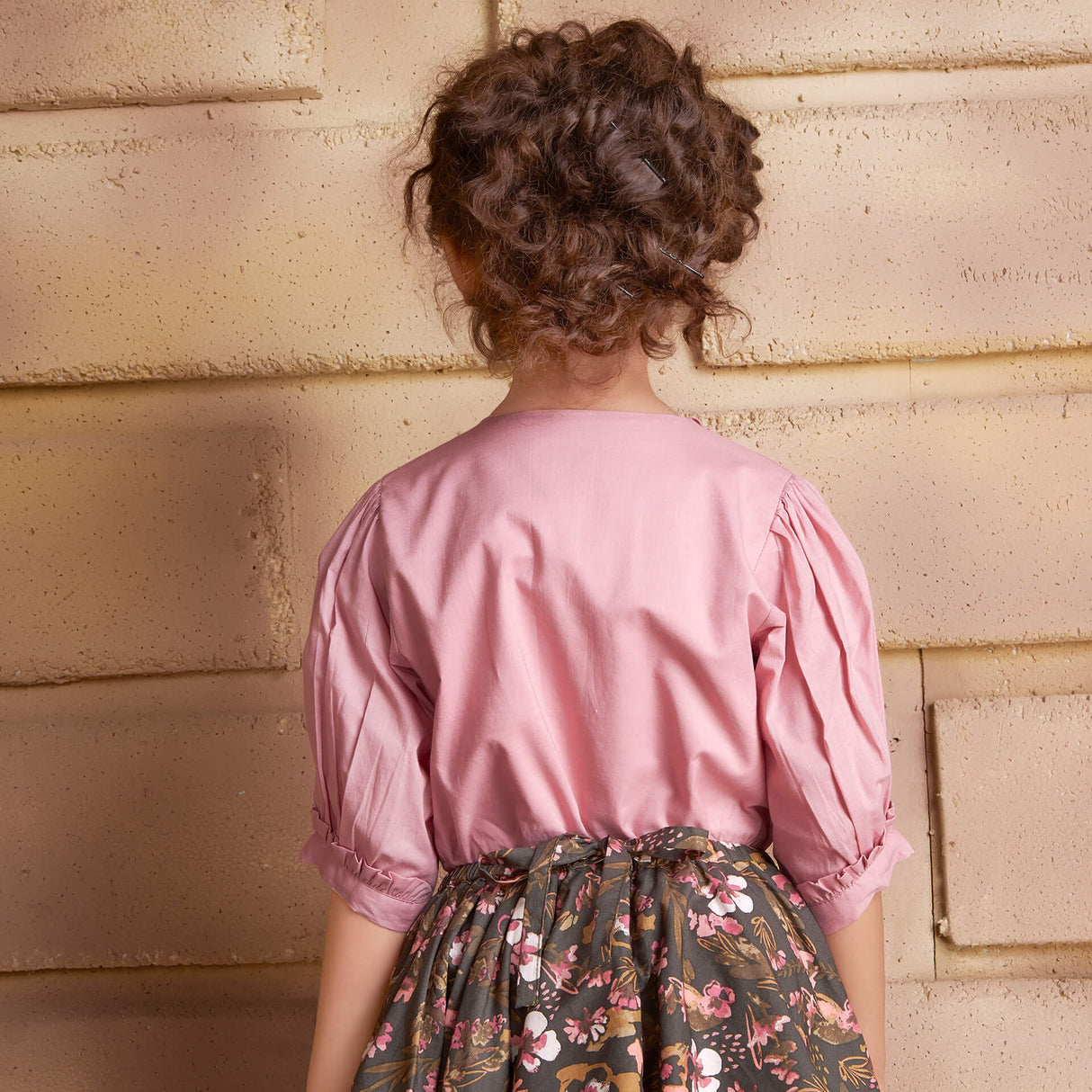 Back view of a girl wearing a pink embroidered blouse and floral printed skirt