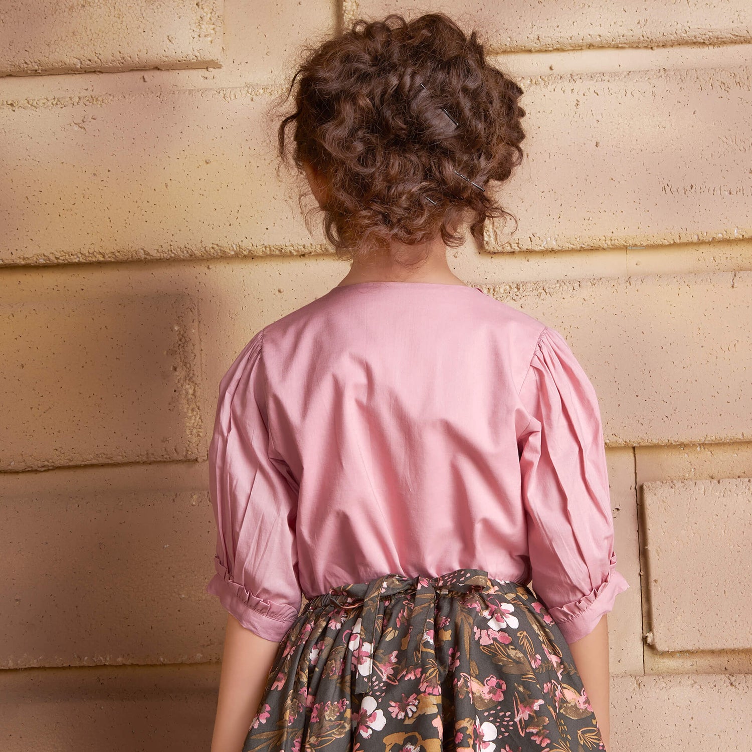 Back view of a girl wearing a pink embroidered blouse and floral printed skirt