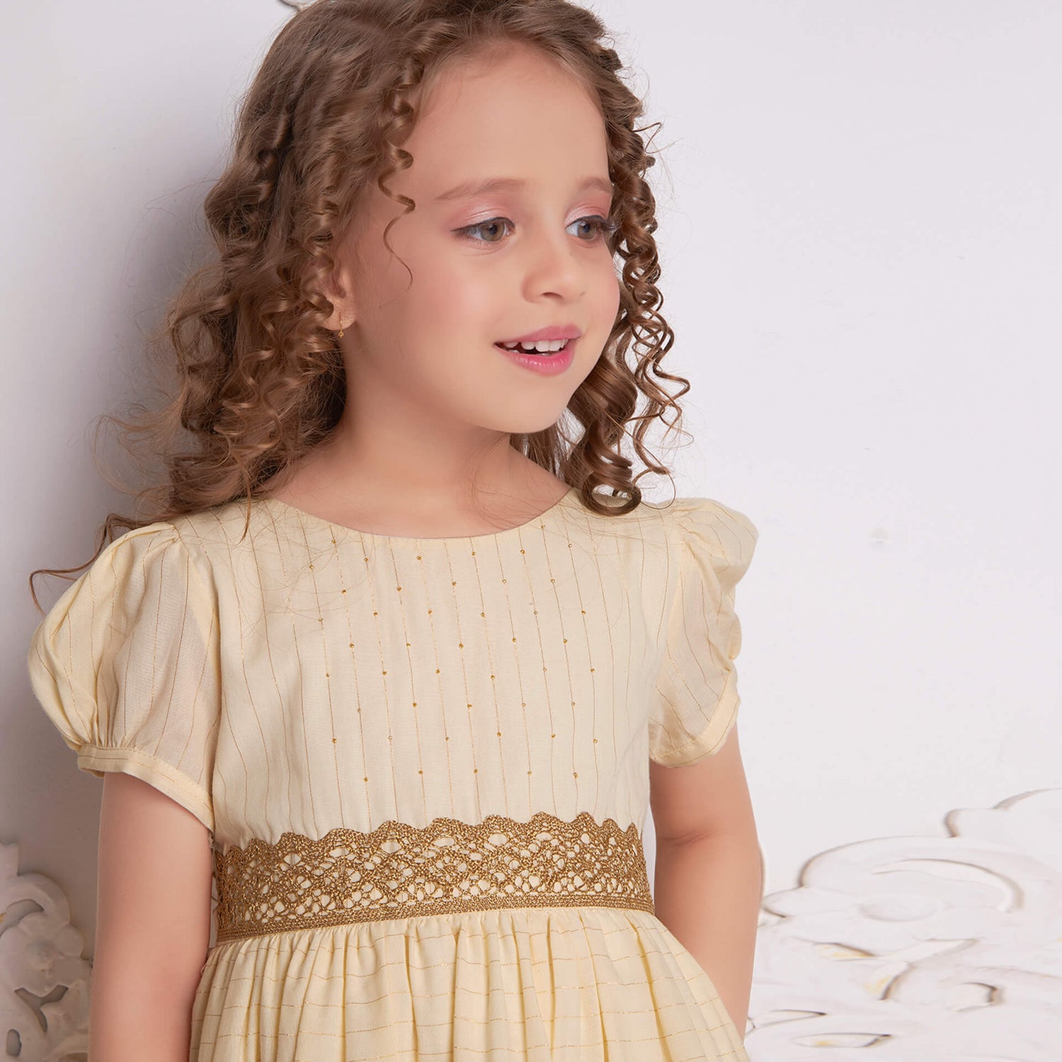 Side view of a girl wearing an ivory lurex beads dress featuring gold metallic lace at the waist