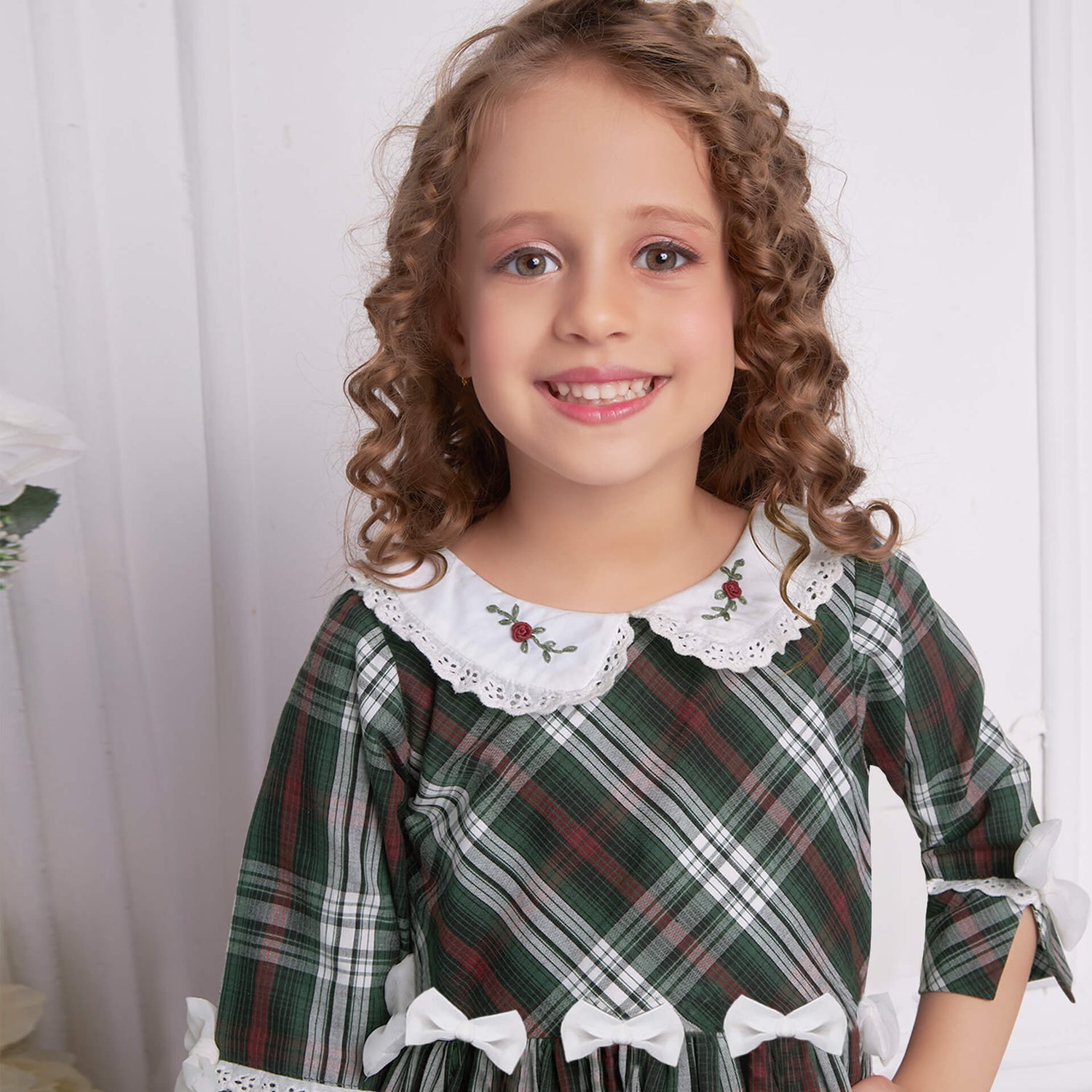 Closeup of a girl in green tartan collar embroidered dress with bows at the waist