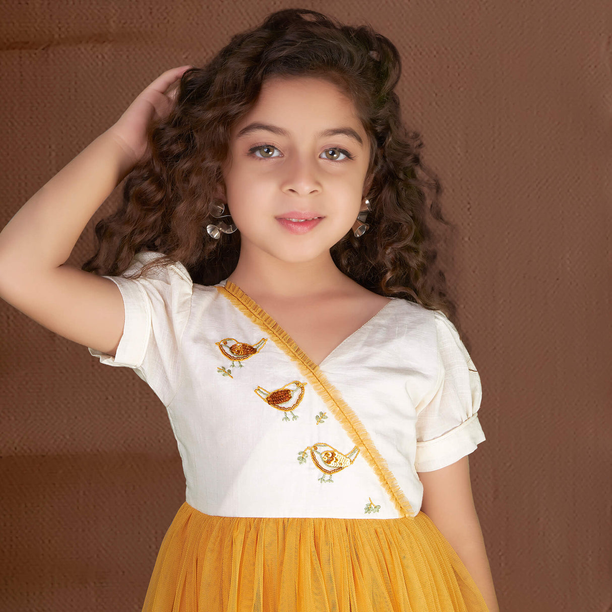 Posing gracefully, a pretty girl showcases a mustard bird embroidered dress