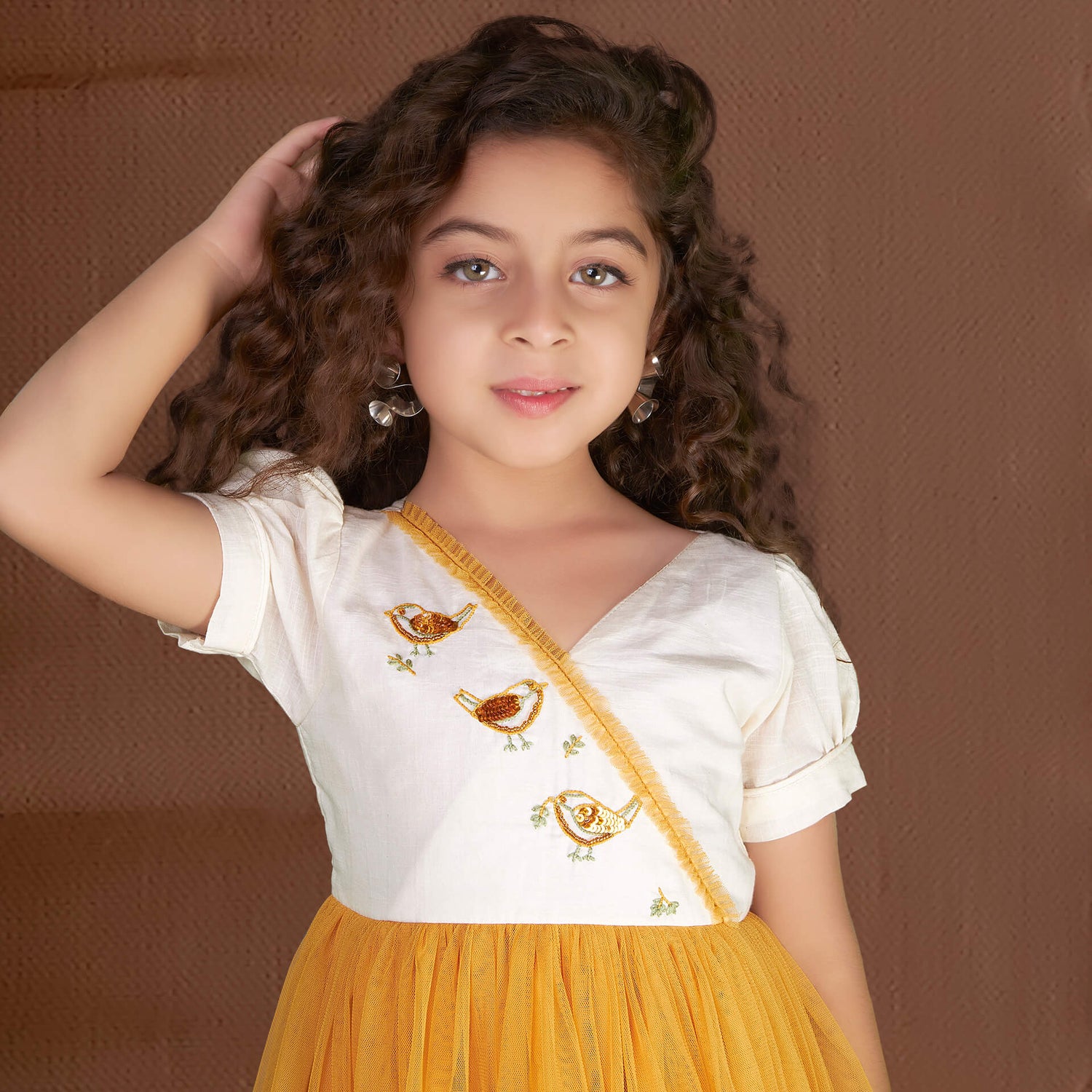 Posing gracefully, a pretty girl showcases a mustard bird embroidered dress