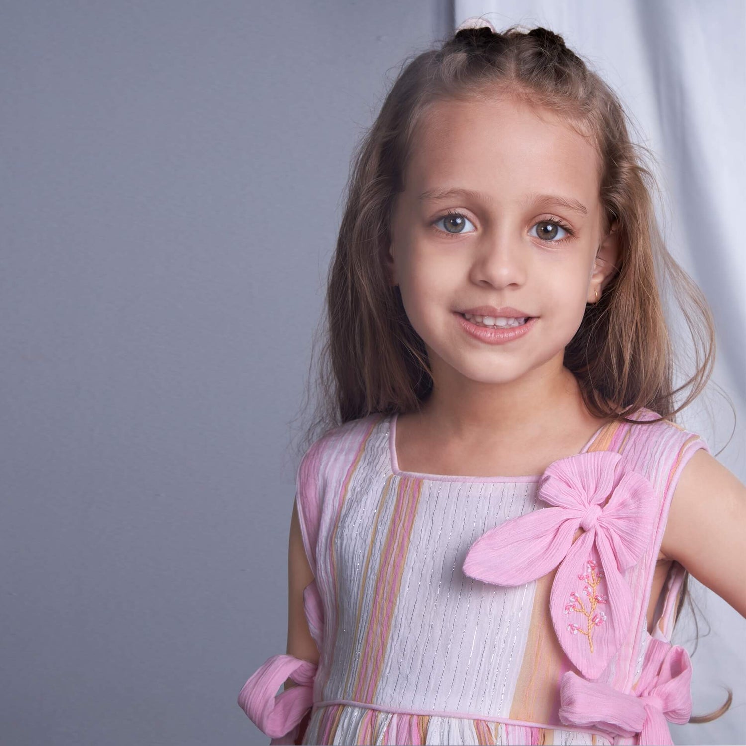 In a focused view, a girl is dressed in a blue lurex dress with an attached embroidered bow near the neckline