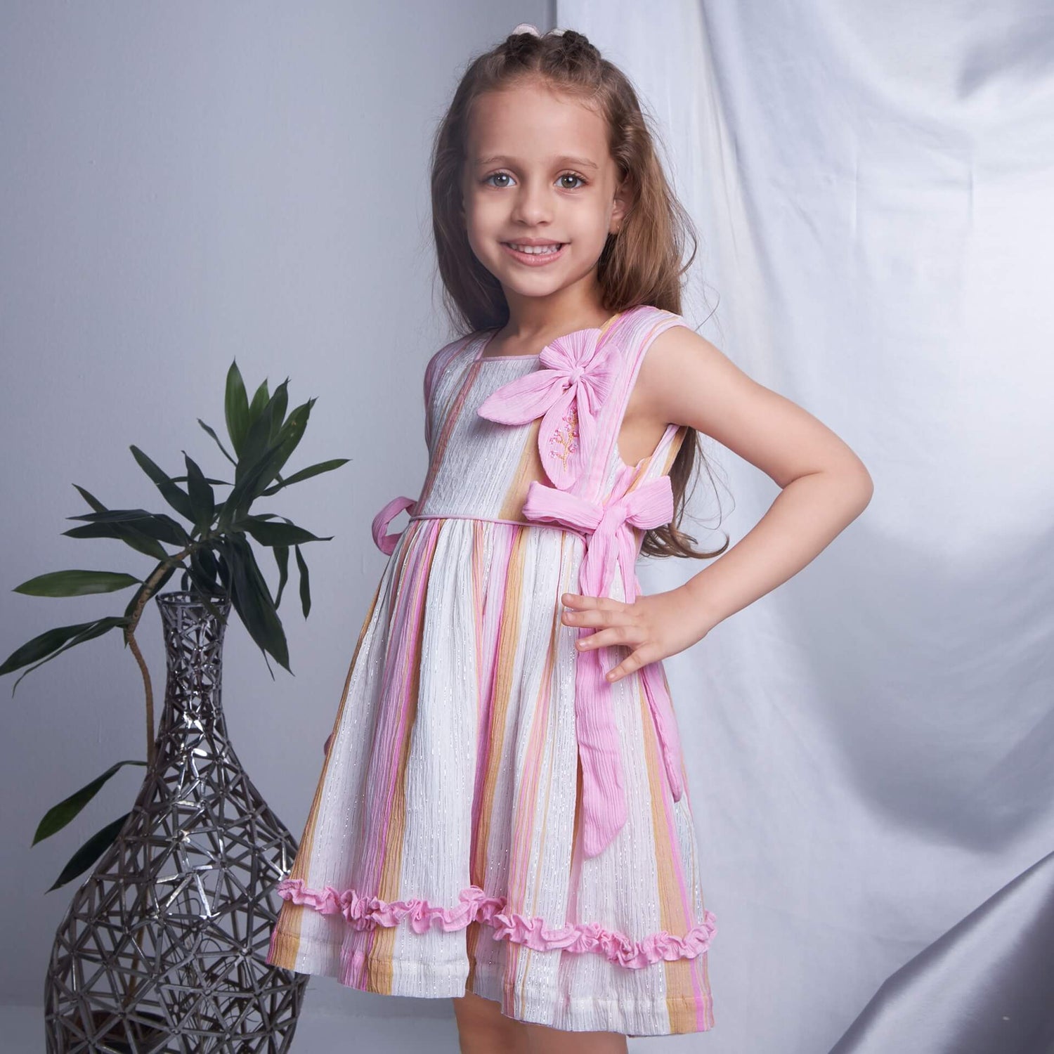 In a side view, a girl wears a pink lurex embroidered bow dress with lace trims