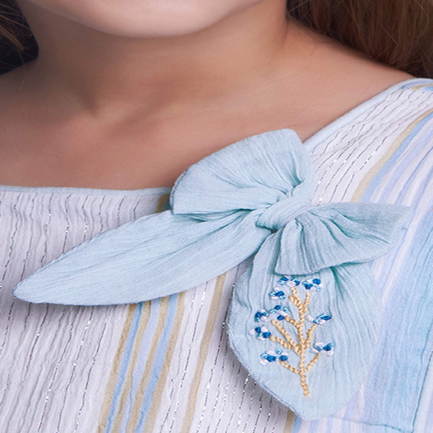 Close-up of bow embroidery on a girl wearing a blue lurex dress