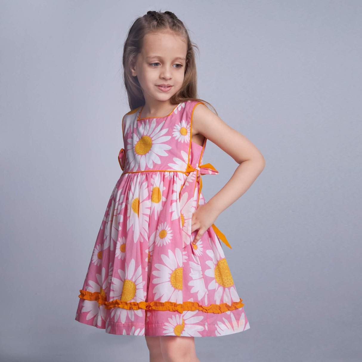 Posing from the side, a little one wears a pink floral dress with side ties in a contrasting tone