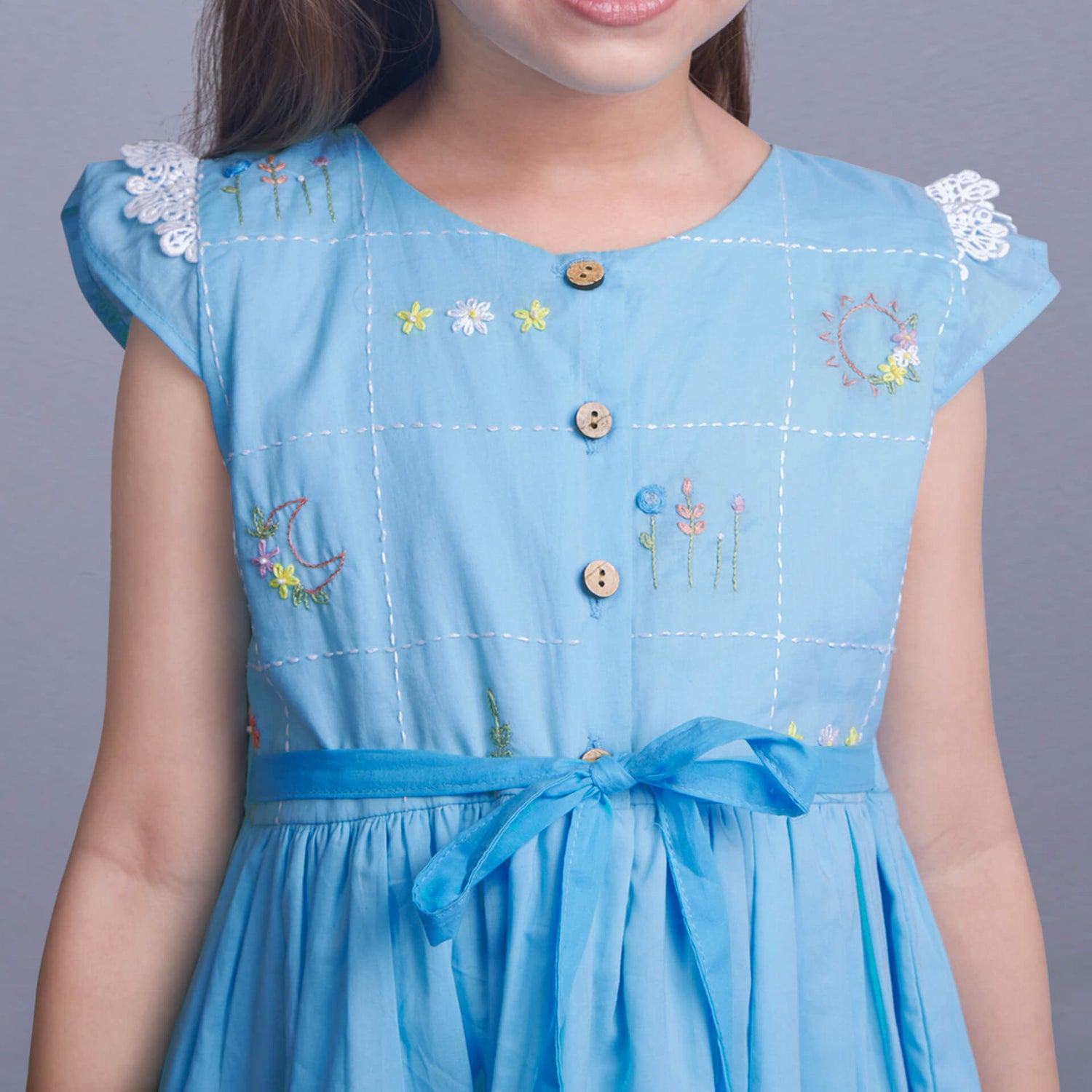 Closeup of hand embroidery on a blue ombre dress with front wood buttons and a tie-up sash