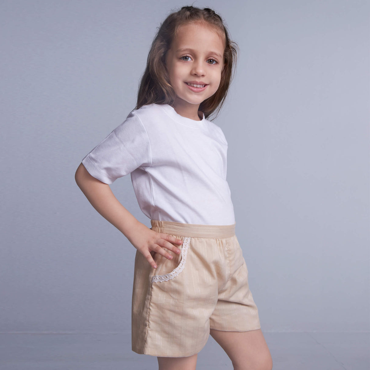 Side pose of a girl wearing white shorts in boats printed fabric, with her hands inserted into the pockets